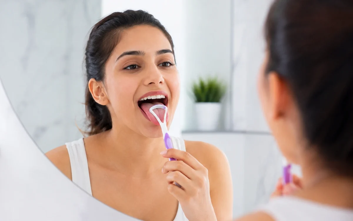 Person using a tongue cleaner during oral hygiene routine at dental clinic consultation